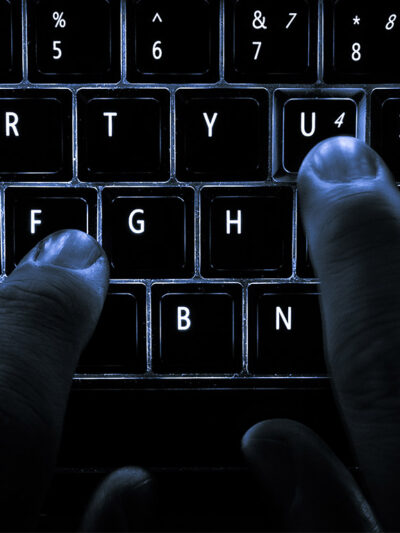 A backlit laptop computer keyboard. Most fingers are on the "home" keys for touch-typing; the 'U' key is being pressed.