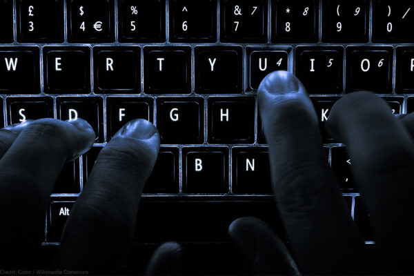 A backlit laptop computer keyboard. Most fingers are on the "home" keys for touch-typing; the 'U' key is being pressed.