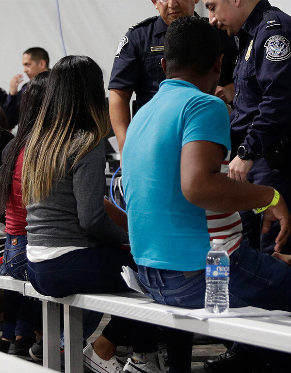 Migrants seated in a processing area at a tent courtroom