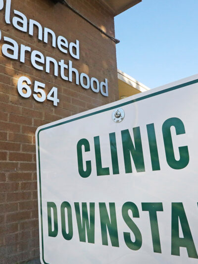 A sign with the text "Clinic Downstairs" outside a Planned Parenthood building