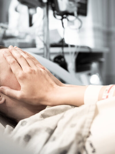 Image of a woman in a hospital bed covering her eyes