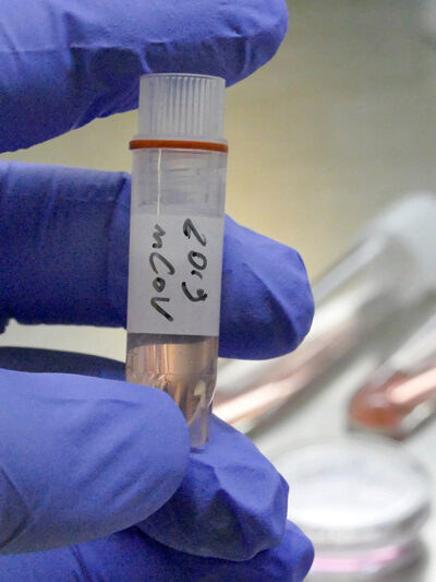 A gloved hand holding a vial of novel coronavirus 2019-nCoV in a laboratory.