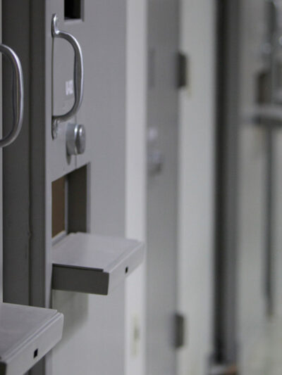 A hallway in a detention center with a line of closed cell doors.