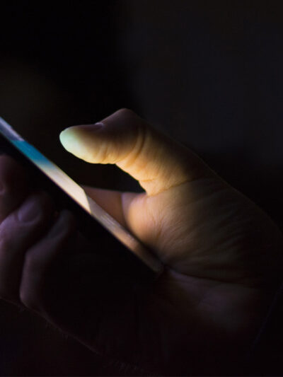 A hand holding a smart phone shrouded in darkness.