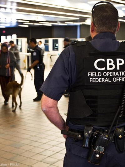 A CBP officer watches over travellers at an airport.