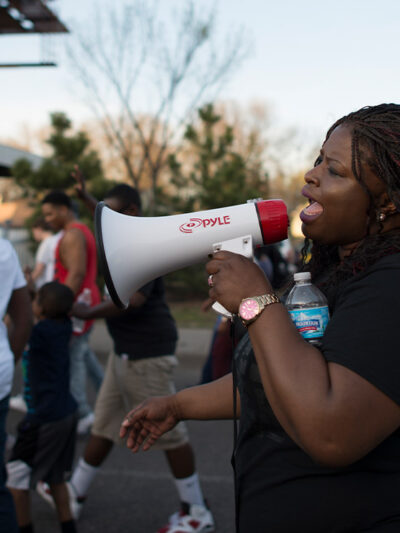 A Black woman using a megaphone at a daytime Black Lives Matter march in Minneapolis, Minnesota in response to police shooting of 18-year-old Tania Harris.