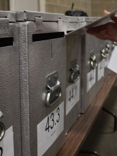 An election worker inserting a ballot into a locked ballot box.