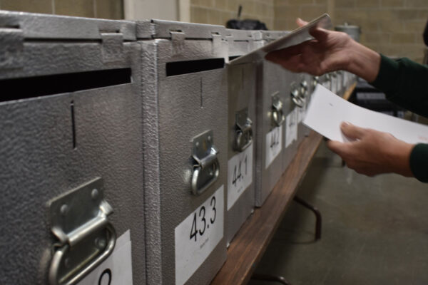 An election worker inserting a ballot into a locked ballot box.