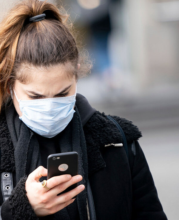 A woman wearing a mask looks at her smartphone.
