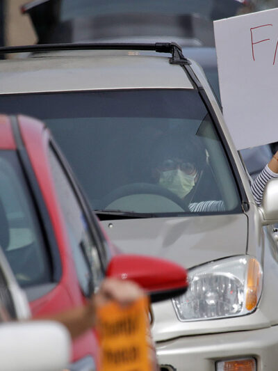 A demonstrator holds a sign with the text "Free Them All" in a car-based protest to demand the release of immigrants in California detention centers over COVID-19 concerns.
