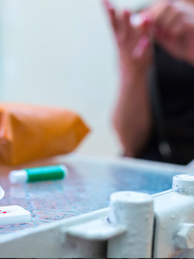 A gloved hand adds reagent to a COVID-19 serological antibody test with the patient sitting nearby.