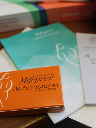 A desk with a box of Mifepristone, an information pamphlet, and a doctor's prescription pad.