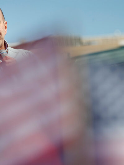 Anthony Romero speaks in the background while mini American flags wave blurred in the foreground.