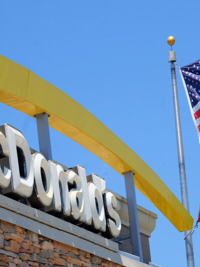 McDonalds logo besides the company flag and the American flag on a flagpole outside of the restaurant chain.