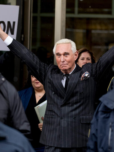 Roger Stone leaving federal court with raised arms wide and flashing two V-shaped hand signs.