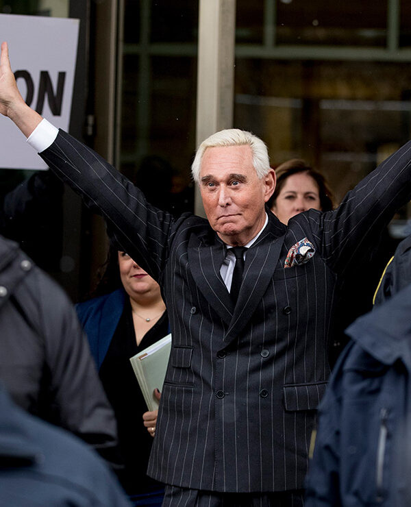 Roger Stone leaving federal court with raised arms wide and flashing two V-shaped hand signs.