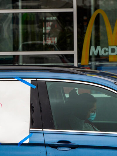 A protester in a car with a sign reading "Worker Health is Public Health" at a socially distanced protest.