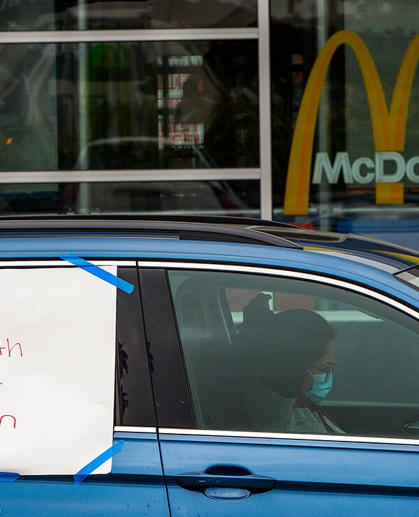 A protester in a car with a sign reading "Worker Health is Public Health" at a socially distanced protest.