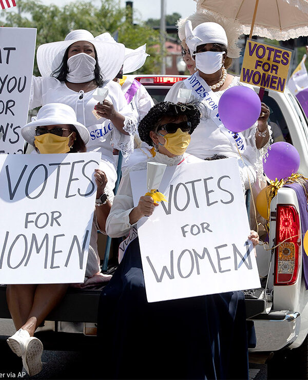 Demonstrators in period clothing with signs advocating for women's suffrage.