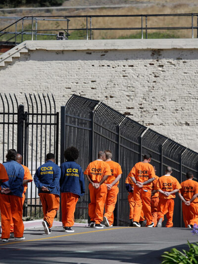 A row of general population inmates, handcuffed and in orange jumpsuits, walk in a line at San Quentin State Prison.
