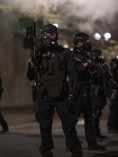 Police in Portland wear riot gear and armed with guns as smoke fills the streets.