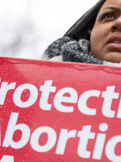 A woman holds a "protecting abortion access" sign in the rain.