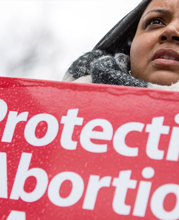 A woman holds a "protecting abortion access" sign in the rain.