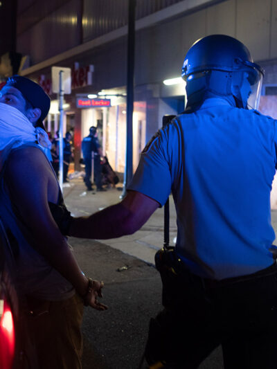 A police officer holds a man against the back of his police car during a night of unrest in downtown Minneapolis.
