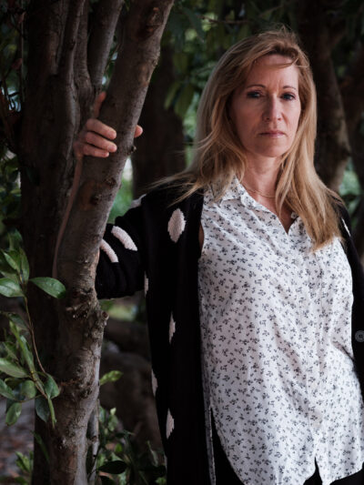 Kristen DiAngelo, sex worker and activist, in white shirt standing with arm on a tree branch