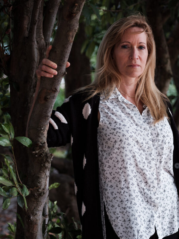Kristen DiAngelo, sex worker and activist, in white shirt standing with arm on a tree branch