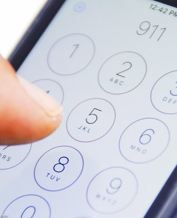 Hand holding smartphone with emergency number 911 on the screen.