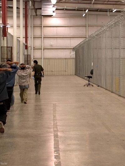 Armed CBP guard watches inmates in a CBP facility