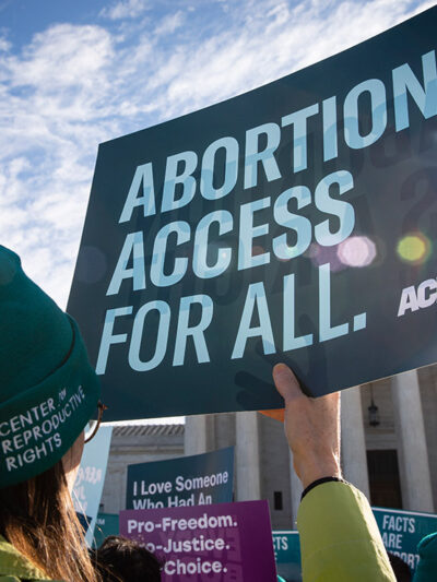 Person holds up ACLU sign that reads "Abortion Access for All" in front of the Supreme Court building.