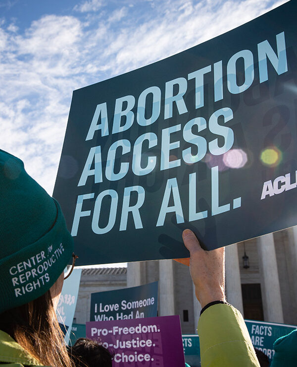 Person holds up ACLU sign that reads "Abortion Access for All" in front of the Supreme Court building.