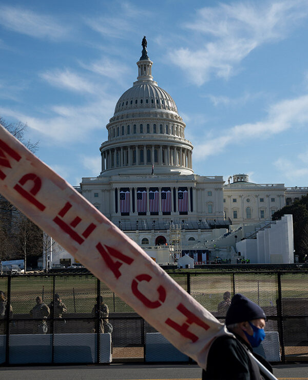A man walks by the U.S. Capitol Building carrying a sign that reads "Impeach"