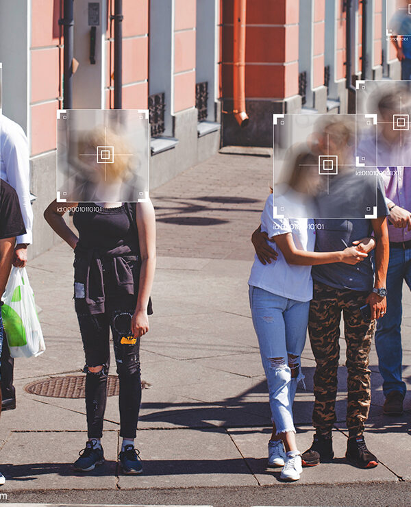 People standing at a crosswalk with face recognition software boxes superimposed over their faces.