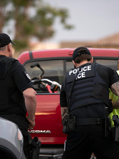 U.S. Immigration and Customs Enforcement (ICE) officers detain someone in front of a red truck.