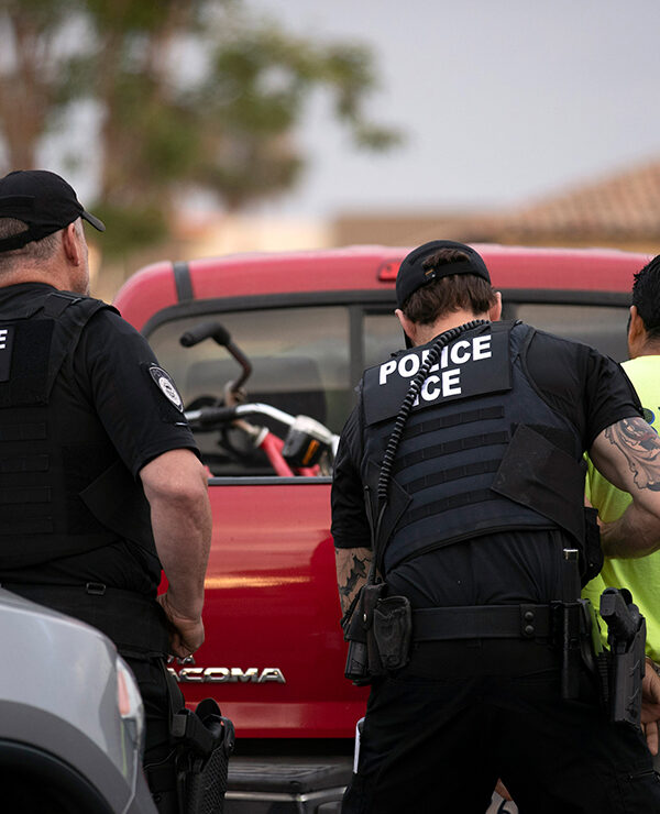 U.S. Immigration and Customs Enforcement (ICE) officers detain someone in front of a red truck.