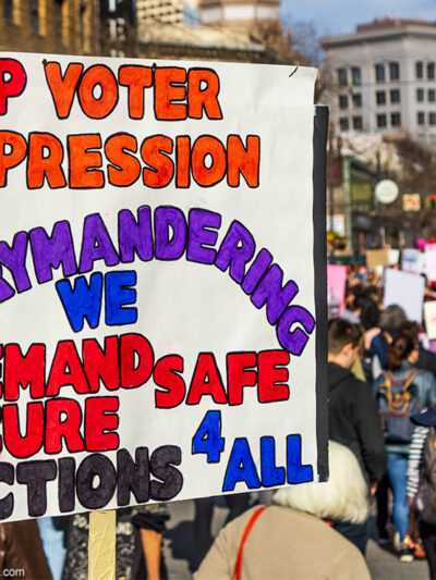 A demonstrator carries a sign demanding an end to gerrymandering and voter suppression.