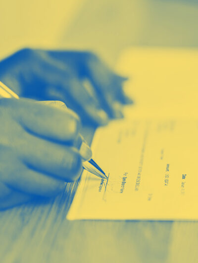 A yellow tinted image on someone signing a check on a desk.