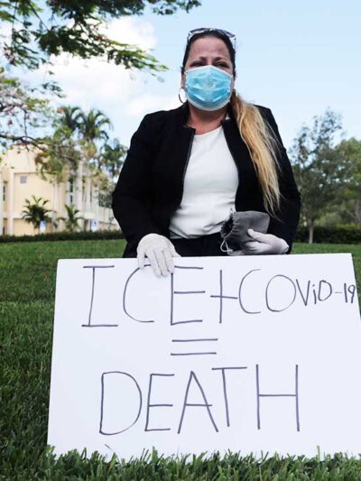 A woman wears a protective face mask and gloves as she protests outside of a U.S. Immigration and Customs Enforcement field office Friday, May 29, 2020, in Plantation, Fla.