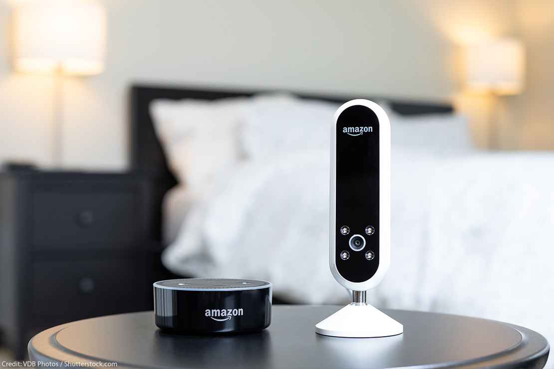 Amazon camera and Amazon Alexa speaker next to each other on a bedside table.