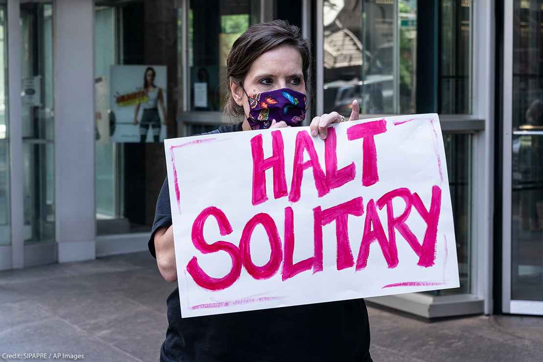 Woman holds sign that reads "halt solitary" as demand to end solitary confinement in prisons