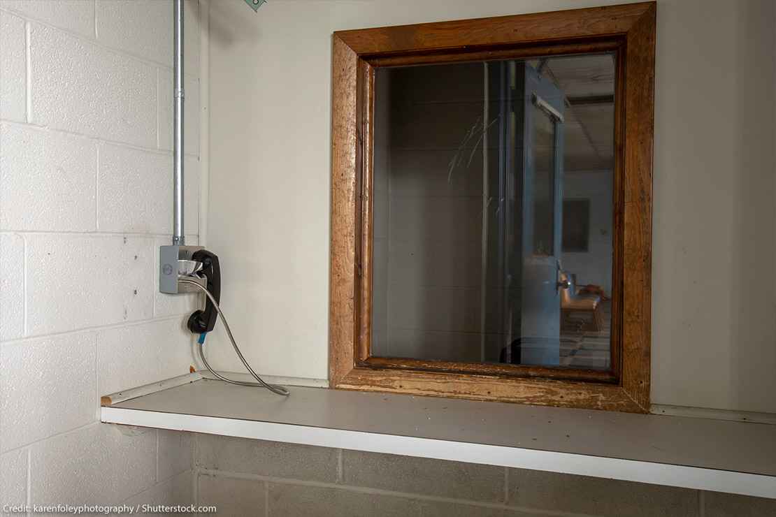 Phone next to window used by visitors to prison to communicate with inmates behind glass.