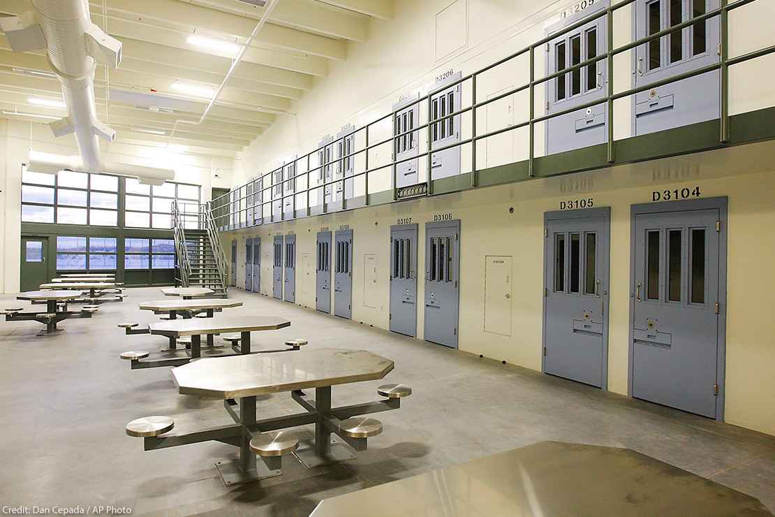 An empty cell block in a prison with tables and blue doors.