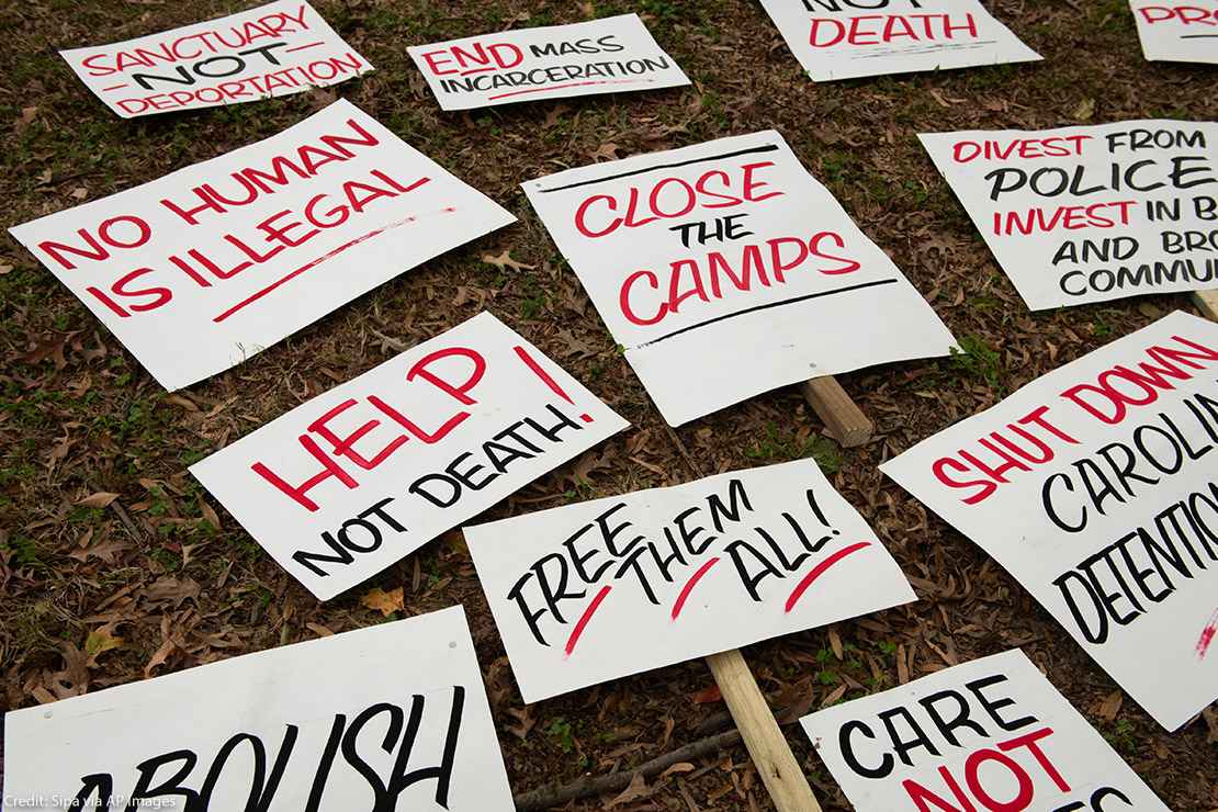 A group of signs on the ground protesting harmful immigration policies, some of which read “No Human Is Illegal,” and “Help Not Death.”