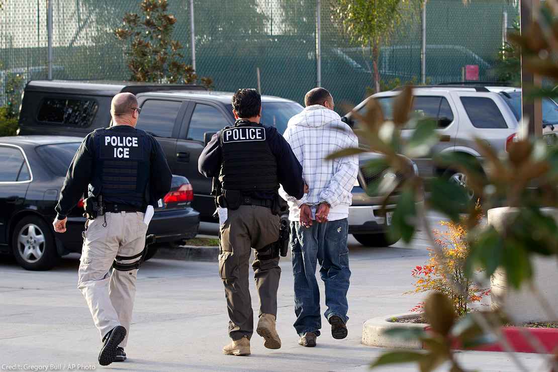 Two Immigration and Customs Enforcement (ICE) agents take a person into custody