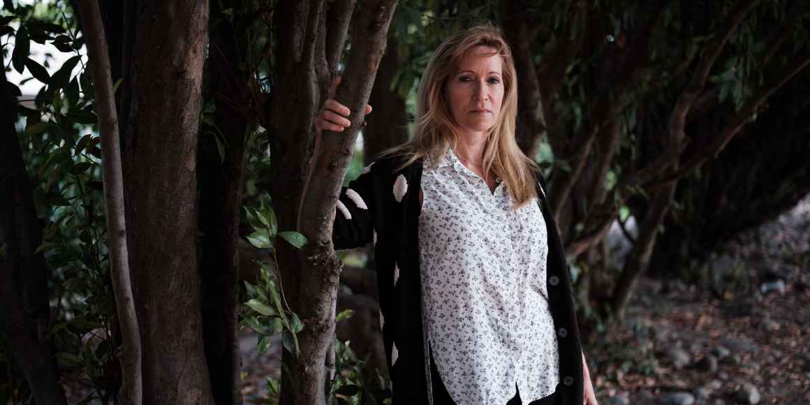 Kristen DiAngelo, sex worker and activist, in white shirt standing with arm on a tree branch