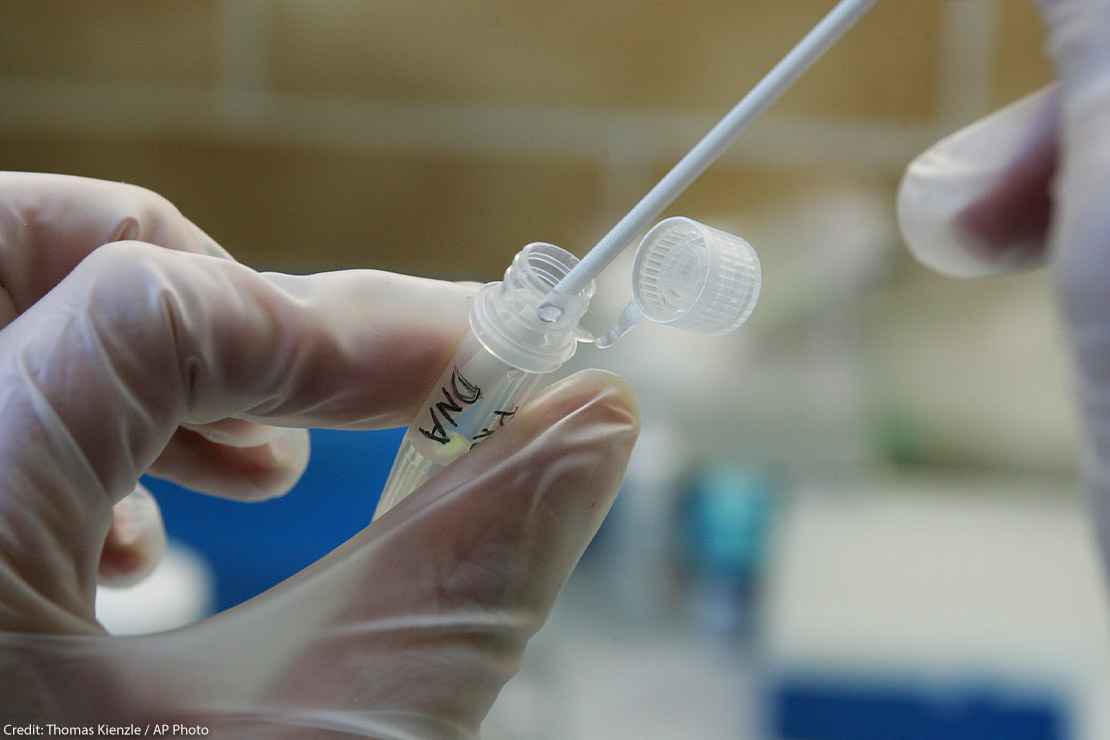 Chemist testing a DNA sample tube in a lab with a cotton swab. Tube labeled DNA.