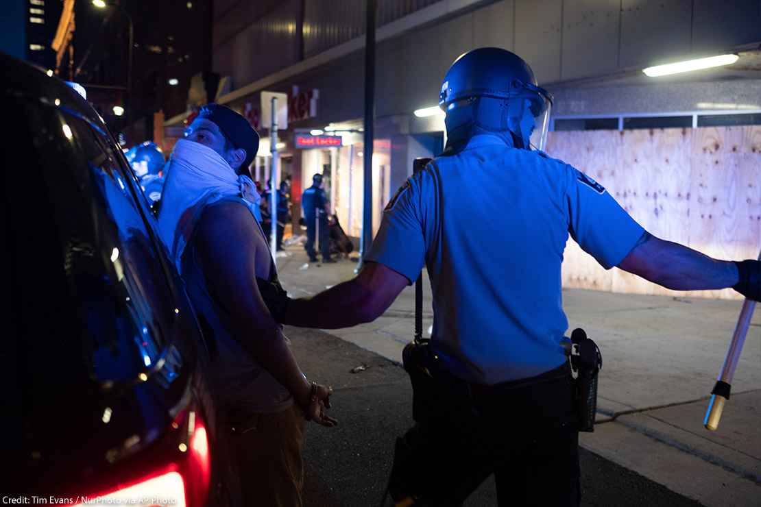 A police officer holds a man against the back of his police car during a night of unrest in downtown Minneapolis.